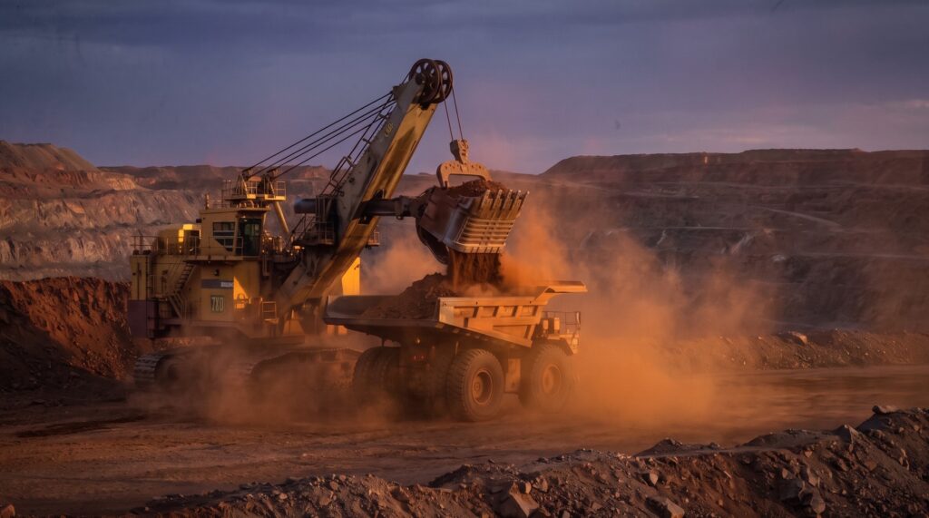 Excavator loading a haul truck at a mine site at dusk, cropped to remove vintage frame border